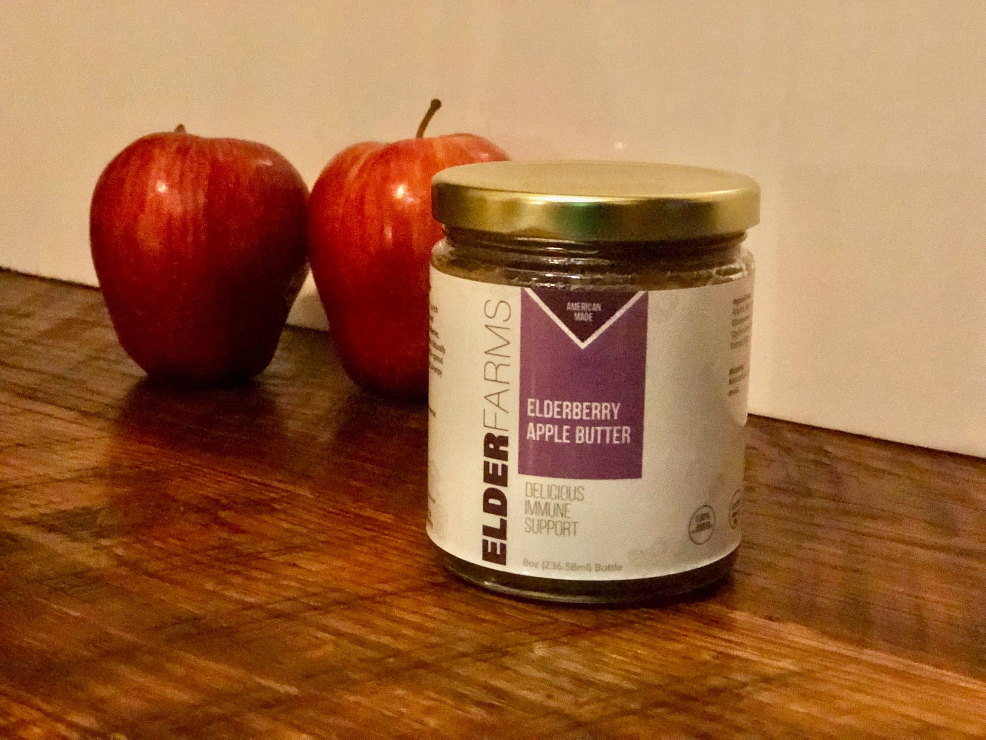 Jar of Elderberry Farms apple butter on a wooden surface with two red apples.