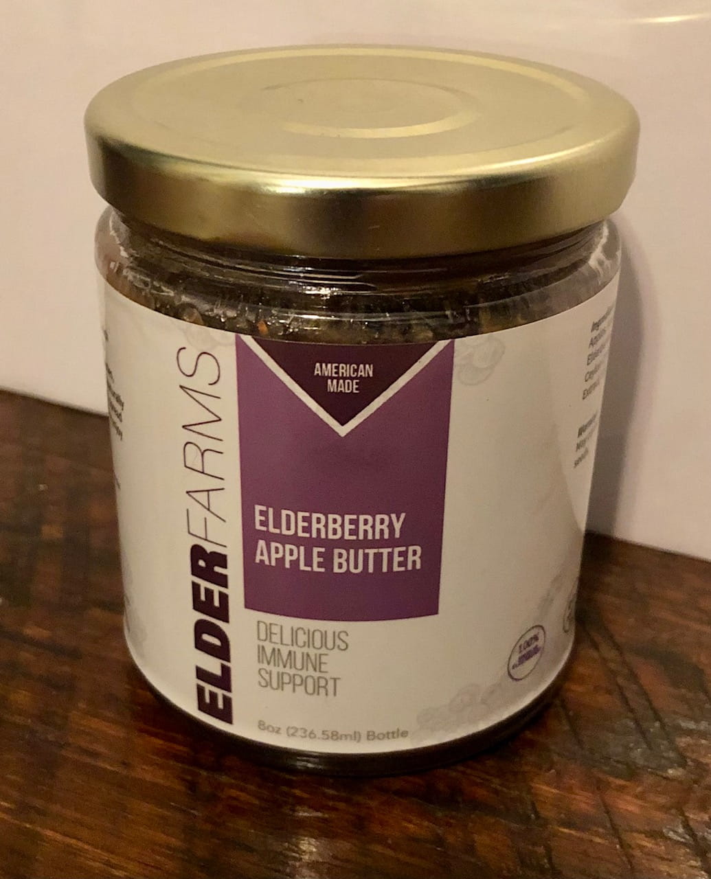 Jar of Elderberry Apple Butter with gold lid on a wooden surface