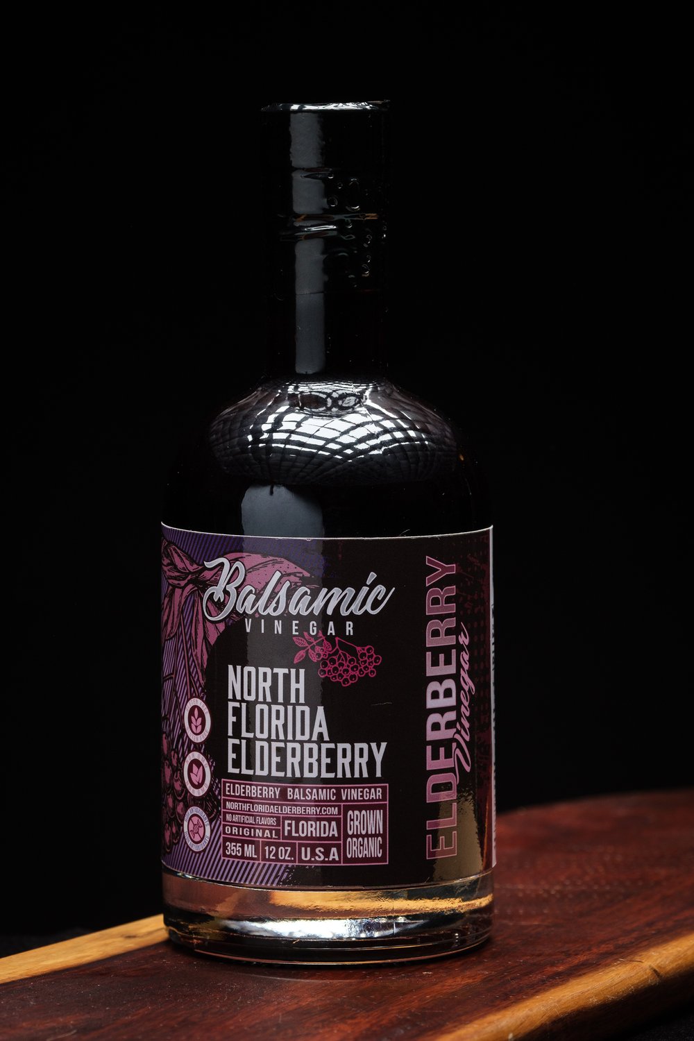 Bottle of North Florida Elderberry Balsamic Vinegar on a wooden surface with a dark background
