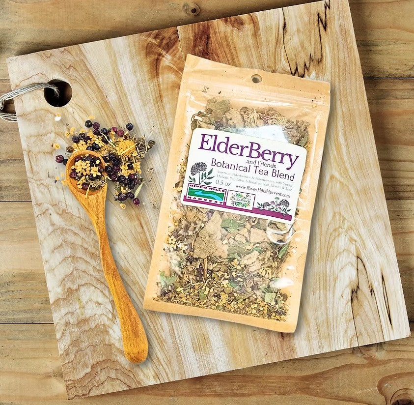 Elderberry botanical tea blend package on a wooden cutting board with a wooden spoon and dried herbs.