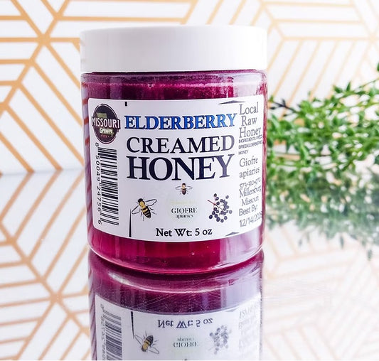 Jar of Elderberry Creamed Honey with a label on a reflective surface.