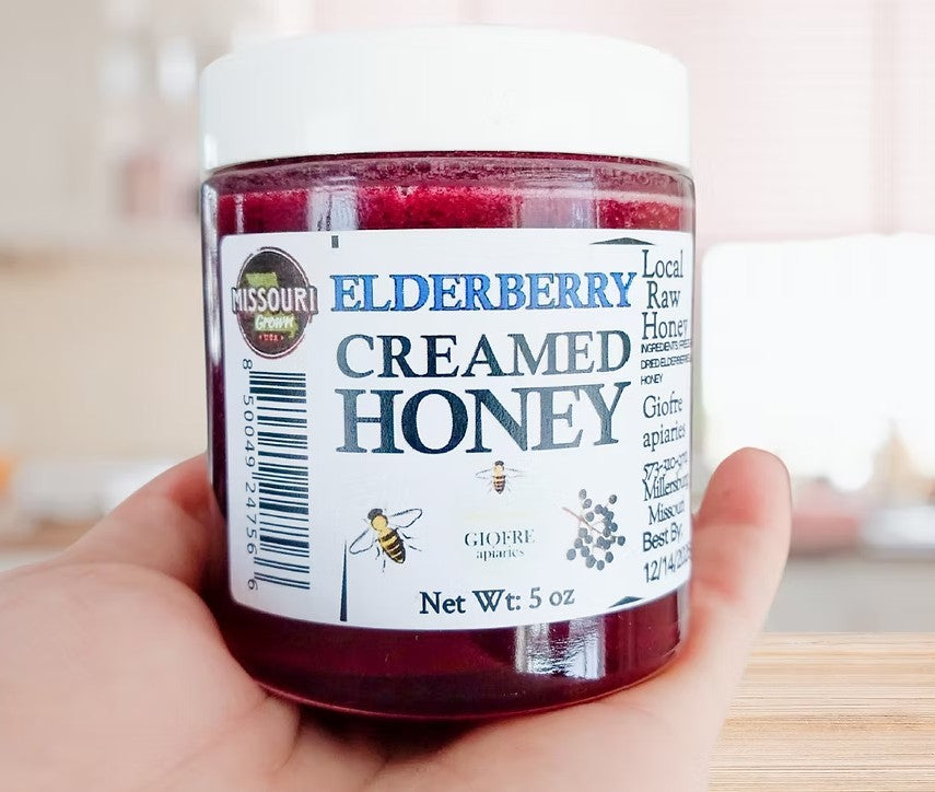 Jar of creamed honey held by a hand with a blurred background