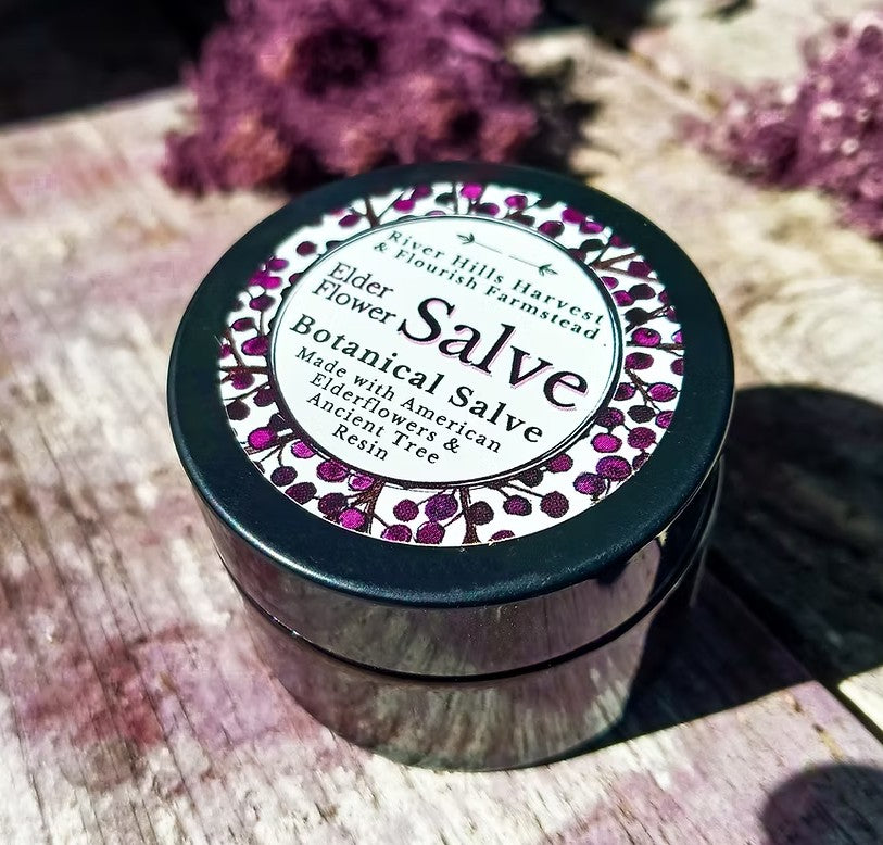 Botanical salve container with floral design on lid, placed on a textured surface with flowers in the background.