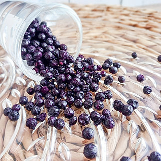 Purple elderberries spilling out of a transparent container onto a woven surface