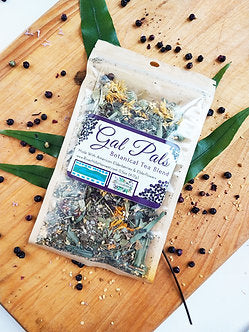 Gal Pal's Botanical Tea Blend package on a wooden board with tea leaves and herbs.