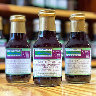 Three bottles of River Hills Harvest Health Cordial Elderberry Juice on a wooden surface.