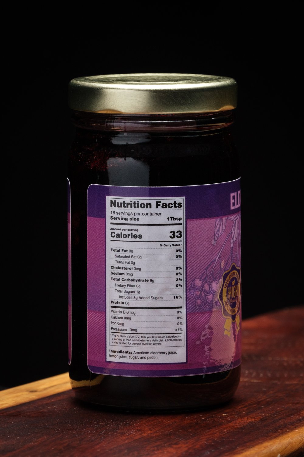 Jar of elderberry jelly with a purple ingredient label on a wooden surface